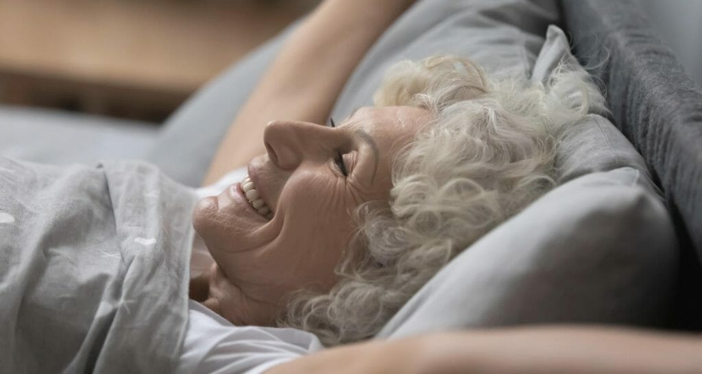 Äldre kvinna som ler i sängen