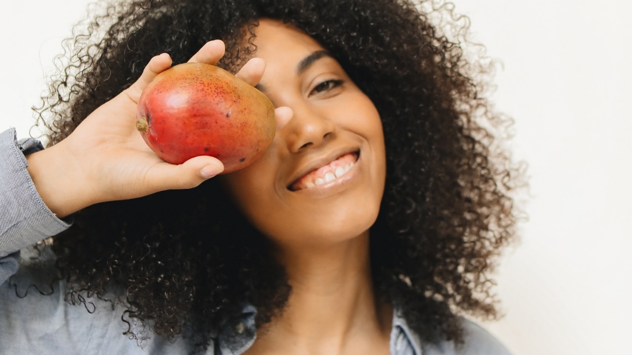 Kvinna i naturligt ljus med en mango, fokus på hud och lyster